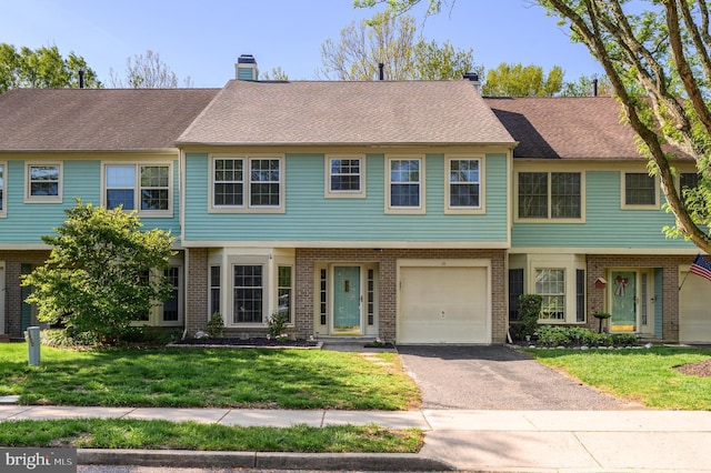 townhome / multi-family property featuring a chimney, driveway, a front lawn, and brick siding