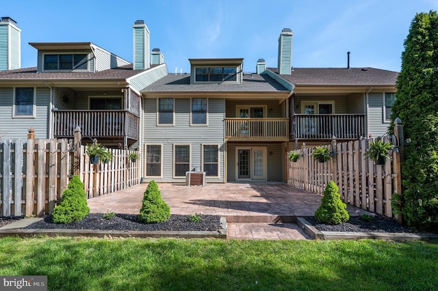 rear view of house featuring fence, a chimney, a balcony, and a patio area