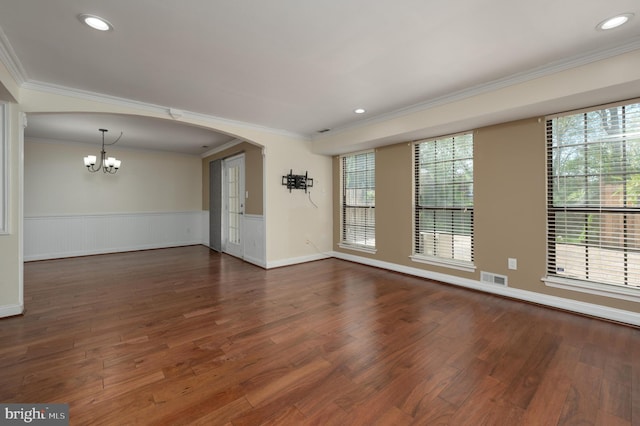 unfurnished room featuring an inviting chandelier, ornamental molding, wood finished floors, and visible vents