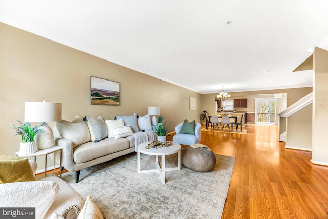 living area with crown molding, an inviting chandelier, stairs, light wood finished floors, and baseboards