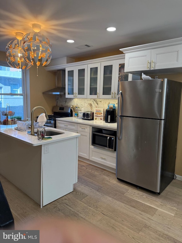 kitchen featuring wall chimney exhaust hood, white cabinetry, visible vents, a sink, and stainless steel appliances