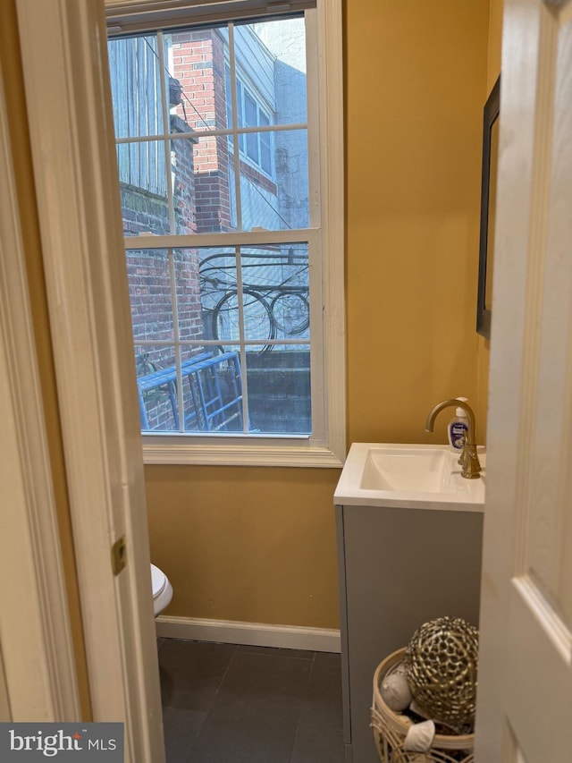 half bathroom with toilet, tile patterned flooring, baseboards, and vanity