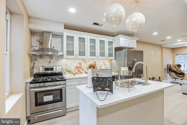 kitchen featuring wall chimney range hood, light wood-style flooring, backsplash, visible vents, and appliances with stainless steel finishes