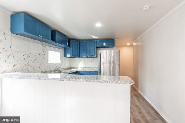 kitchen featuring a sink, a peninsula, light wood-style flooring, freestanding refrigerator, and blue cabinets