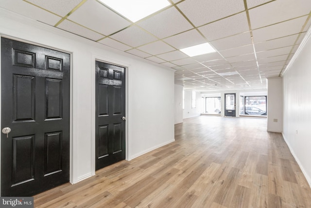 interior space with light wood-style floors, a drop ceiling, and baseboards