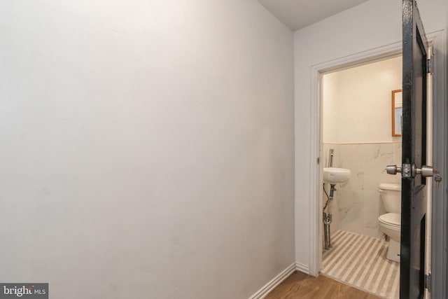 half bathroom with baseboards, tile walls, toilet, wainscoting, and wood finished floors