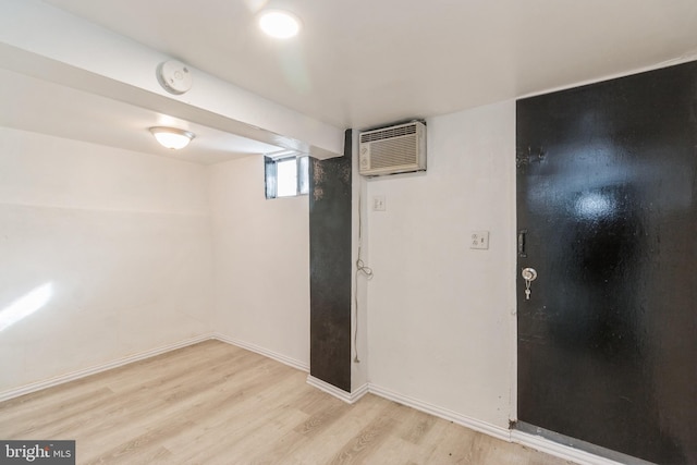 basement with a wall unit AC, light wood finished floors, and baseboards
