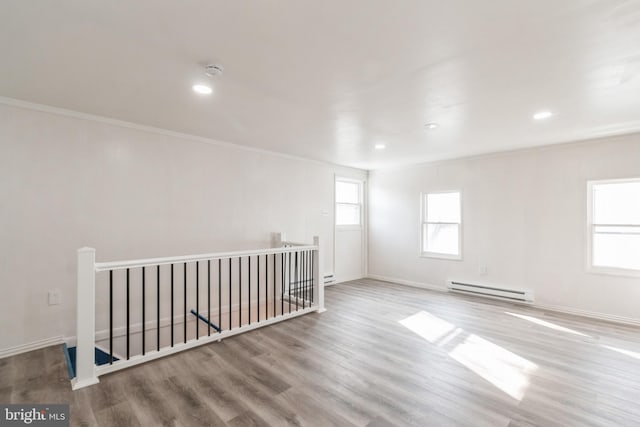 empty room featuring baseboard heating, baseboards, crown molding, and wood finished floors