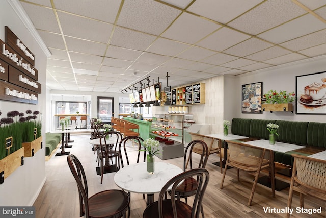 dining space featuring a bar, wood finished floors, and a drop ceiling