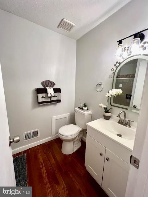 half bathroom with wood finished floors, visible vents, toilet, and vanity