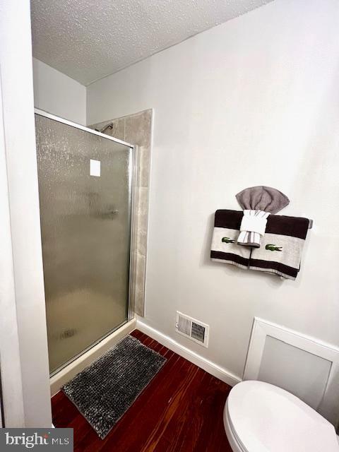 bathroom featuring a shower stall, toilet, visible vents, baseboards, and wood finished floors