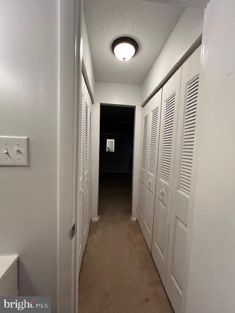 corridor featuring a textured ceiling and light colored carpet