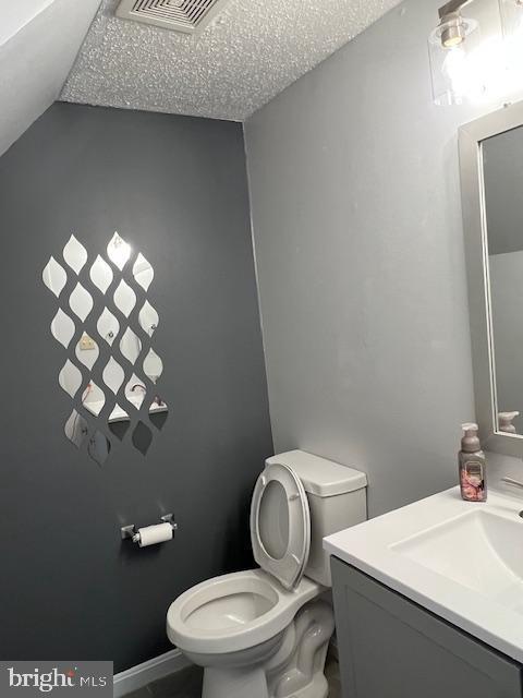 half bathroom featuring visible vents, toilet, a textured ceiling, and vanity