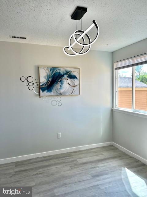 unfurnished dining area with a textured ceiling, wood finished floors, and baseboards