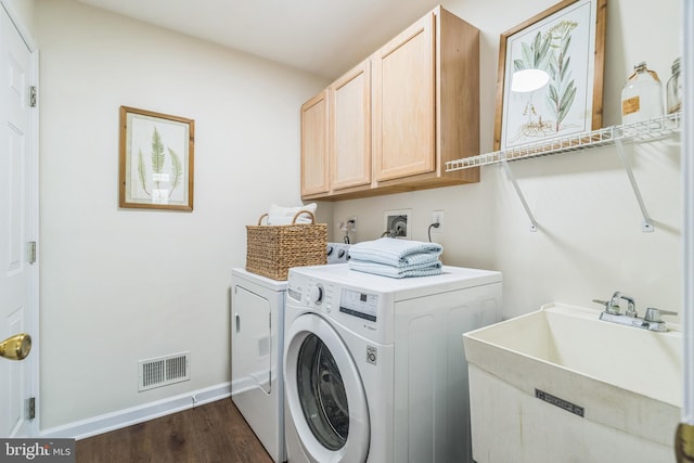 laundry room with washing machine and clothes dryer, a sink, visible vents, cabinet space, and dark wood finished floors