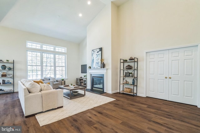 living area featuring a glass covered fireplace, high vaulted ceiling, baseboards, and dark wood finished floors
