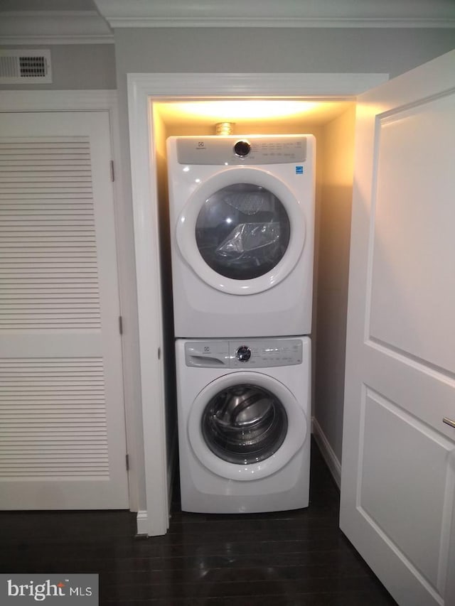 washroom with stacked washer and dryer, laundry area, ornamental molding, visible vents, and dark wood-style floors