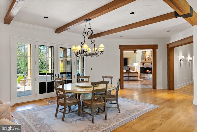 dining area with light wood-style flooring, a chandelier, a warm lit fireplace, and beamed ceiling
