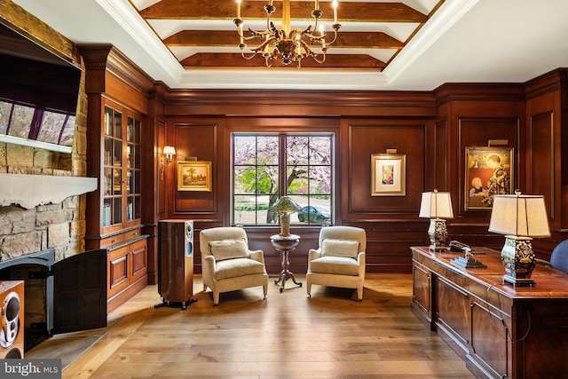 living area with an inviting chandelier, light wood-style floors, crown molding, and a stone fireplace