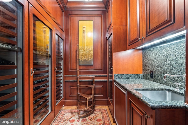 wine area with crown molding, a sink, light wood-style flooring, and a decorative wall