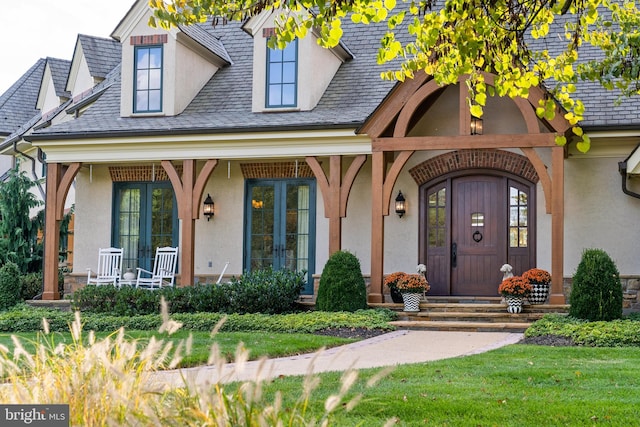 view of exterior entry with a lawn, french doors, covered porch, and stucco siding