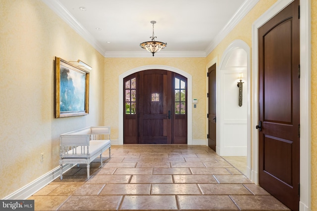 foyer entrance with crown molding, arched walkways, baseboards, stone tile flooring, and a chandelier