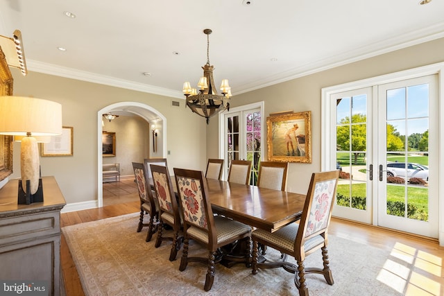 dining area featuring crown molding, a notable chandelier, light wood-style floors, arched walkways, and french doors