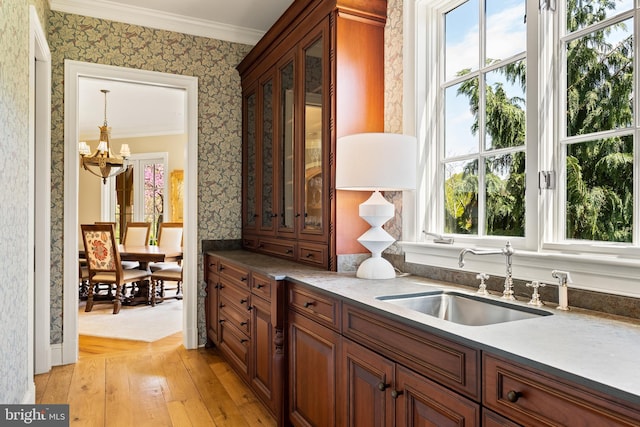 kitchen with a sink, an inviting chandelier, ornamental molding, and wallpapered walls