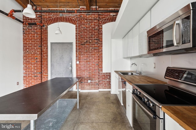 1714 Memphis St Unit 402, Philadelphia, PA 19125 - kitchen with concrete floors, brick wall, white cabinets, stainless steel appliances, and a sink