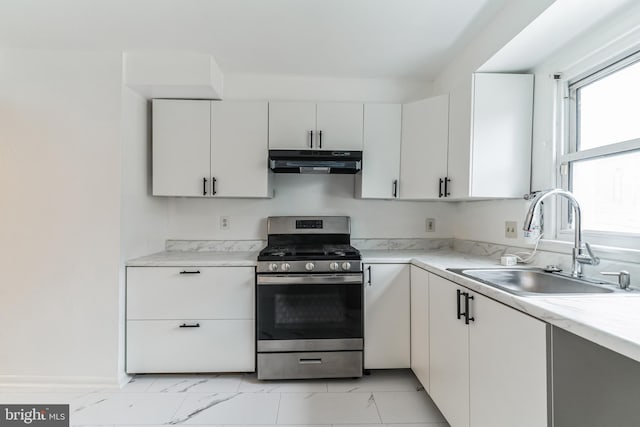 kitchen with stainless steel gas range oven, white cabinetry, under cabinet range hood, marble finish floor, and a sink