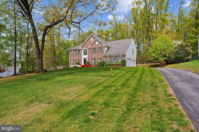 colonial house featuring a front yard, driveway, brick siding, an attached garage, and fence