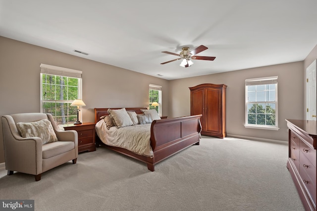 bedroom featuring light colored carpet, visible vents, a ceiling fan, and multiple windows