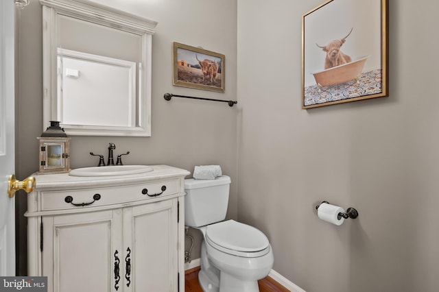 half bath featuring baseboards, wood finished floors, toilet, and vanity