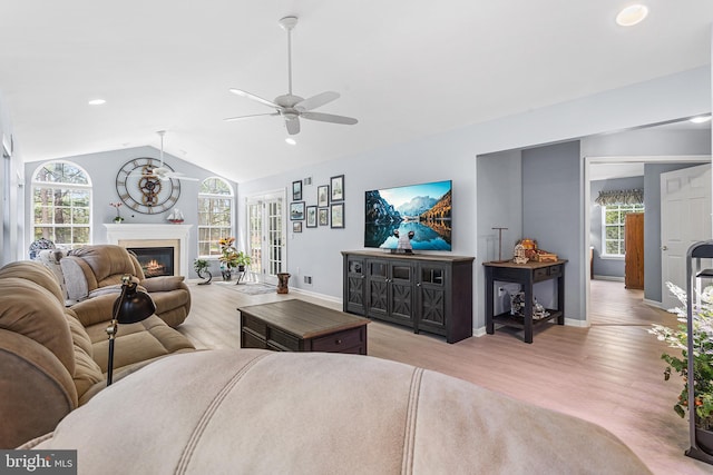 living area with vaulted ceiling, a glass covered fireplace, light wood-type flooring, ceiling fan, and baseboards