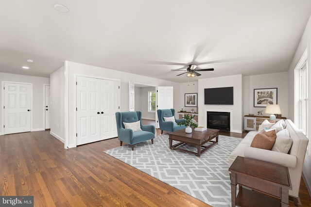 living area featuring wood finished floors, ceiling fan, baseboards, and a glass covered fireplace