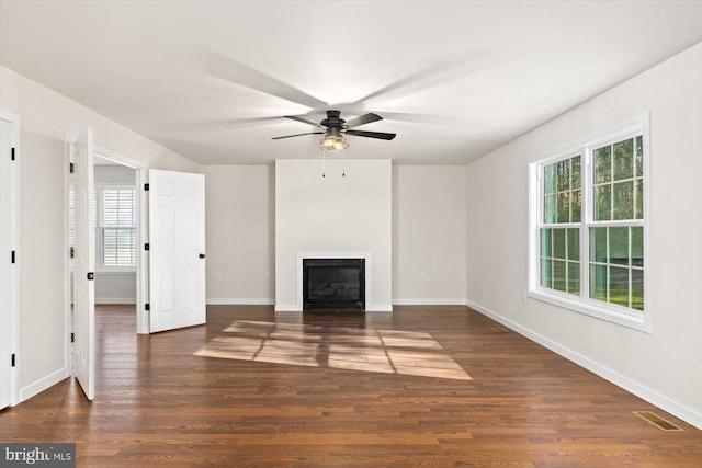 unfurnished living room featuring a ceiling fan, a glass covered fireplace, visible vents, wood finished floors, and baseboards
