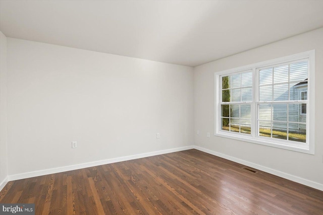 spare room with dark wood-style flooring, visible vents, and baseboards