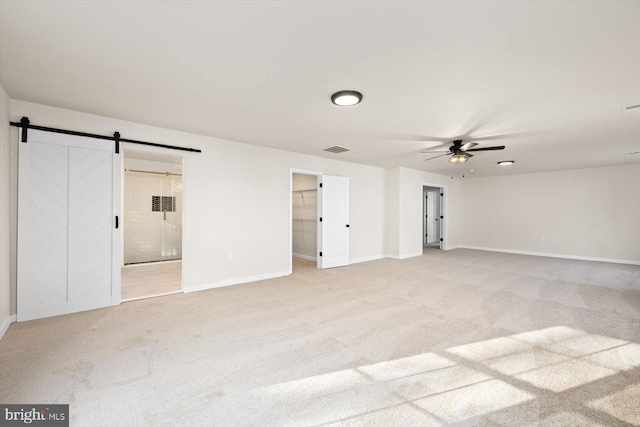 unfurnished bedroom featuring a walk in closet, a barn door, light colored carpet, and baseboards