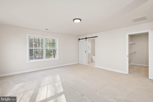 unfurnished bedroom featuring visible vents, baseboards, a barn door, a spacious closet, and light carpet