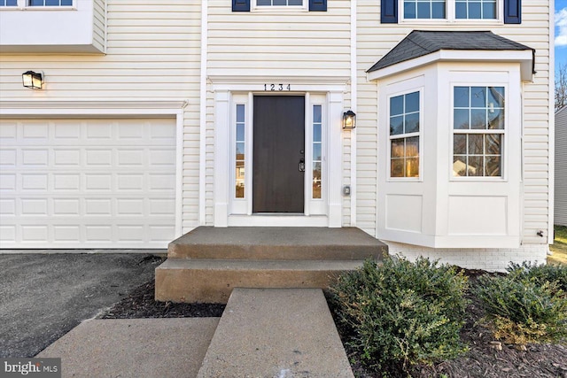 view of exterior entry with an attached garage, a shingled roof, and aphalt driveway