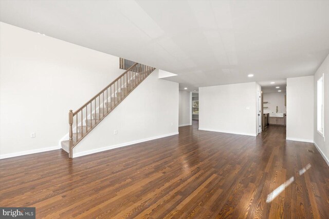unfurnished living room featuring dark wood-style flooring, baseboards, stairway, and recessed lighting