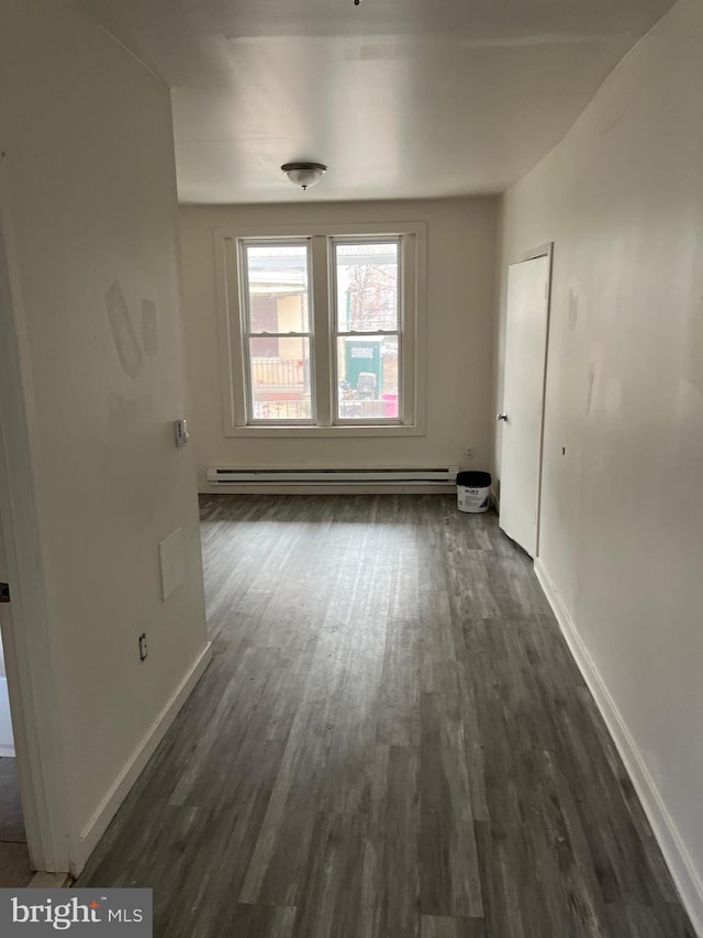 spare room featuring baseboard heating, baseboards, and dark wood finished floors