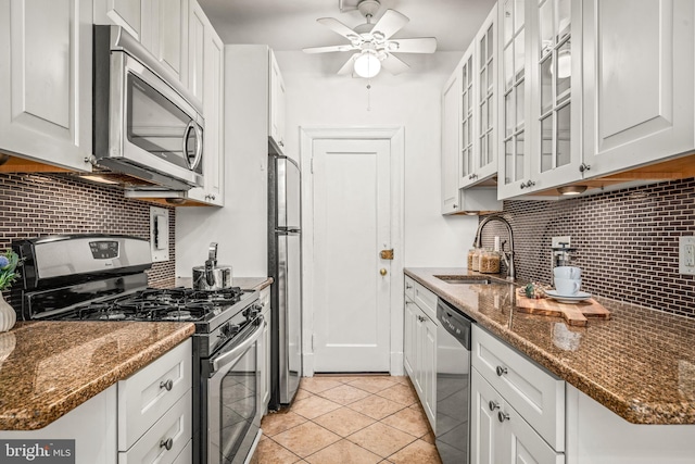 kitchen featuring glass insert cabinets, a sink, ceiling fan, appliances with stainless steel finishes, and decorative backsplash