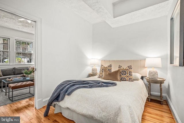 bedroom featuring baseboards, a textured ceiling, and wood finished floors