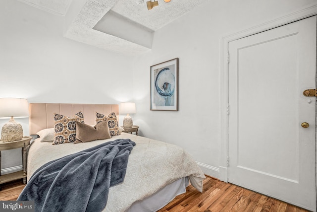 bedroom featuring a textured ceiling, baseboards, and wood finished floors