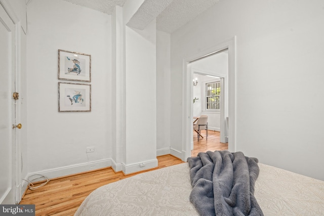 bedroom with a textured ceiling, baseboards, and wood finished floors