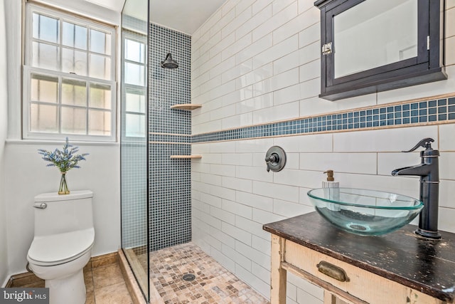 bathroom featuring toilet, tiled shower, vanity, and tile patterned flooring