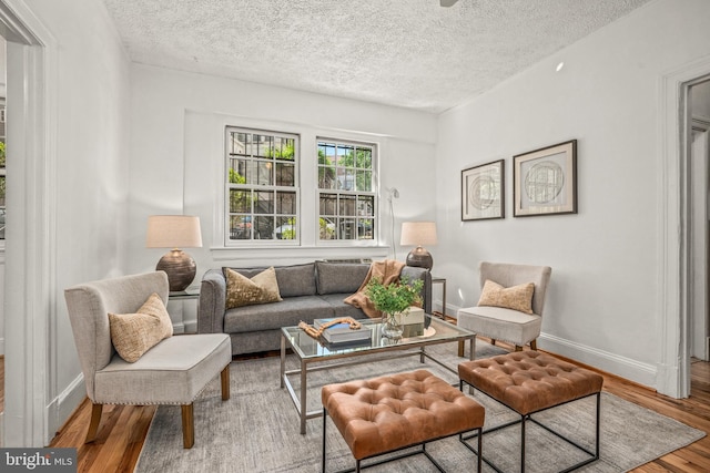 living area with baseboards, a textured ceiling, and wood finished floors