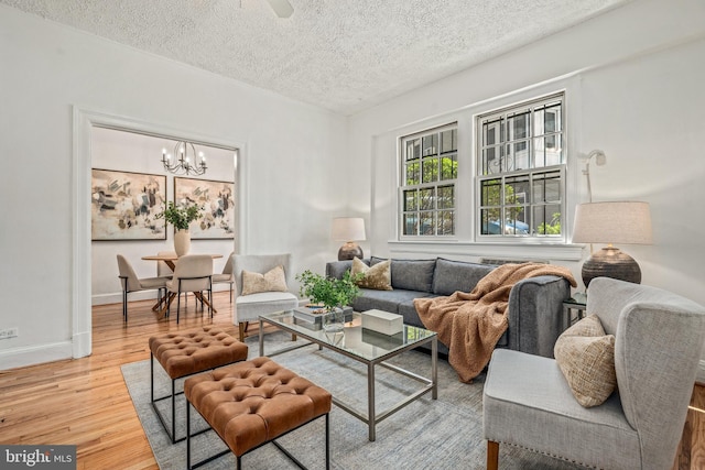 living room with baseboards, light wood-type flooring, a textured ceiling, and ceiling fan with notable chandelier