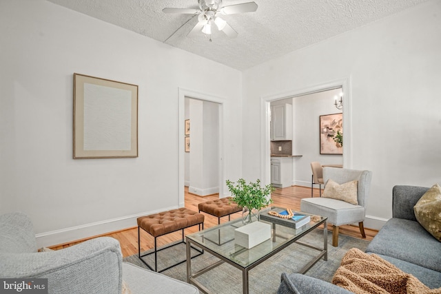 living area with light wood finished floors, a textured ceiling, baseboards, and a ceiling fan